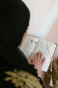 A woman in black hijab reads the Quran indoors, symbolizing faith and spirituality.