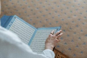 A person holding an open Quran, highlighting religious study or prayer within a serene setting.